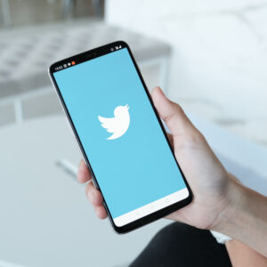 Osoba, trzymająca w dłoni telefon z logo Twittera.