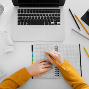 Widok z góry na osobę robiącą notatki przy laptopie.