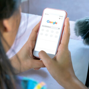 Widok z profilu na osobę, trzymającą telefon z włączoną wyszukiwarką Google