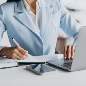 Osoba siedząca przy biurku z laptopem i notatkami.