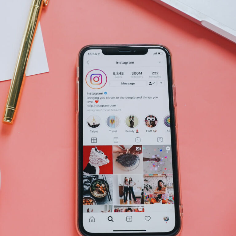 Telefon z włączonym Instagramem, leżący na różowym tle.