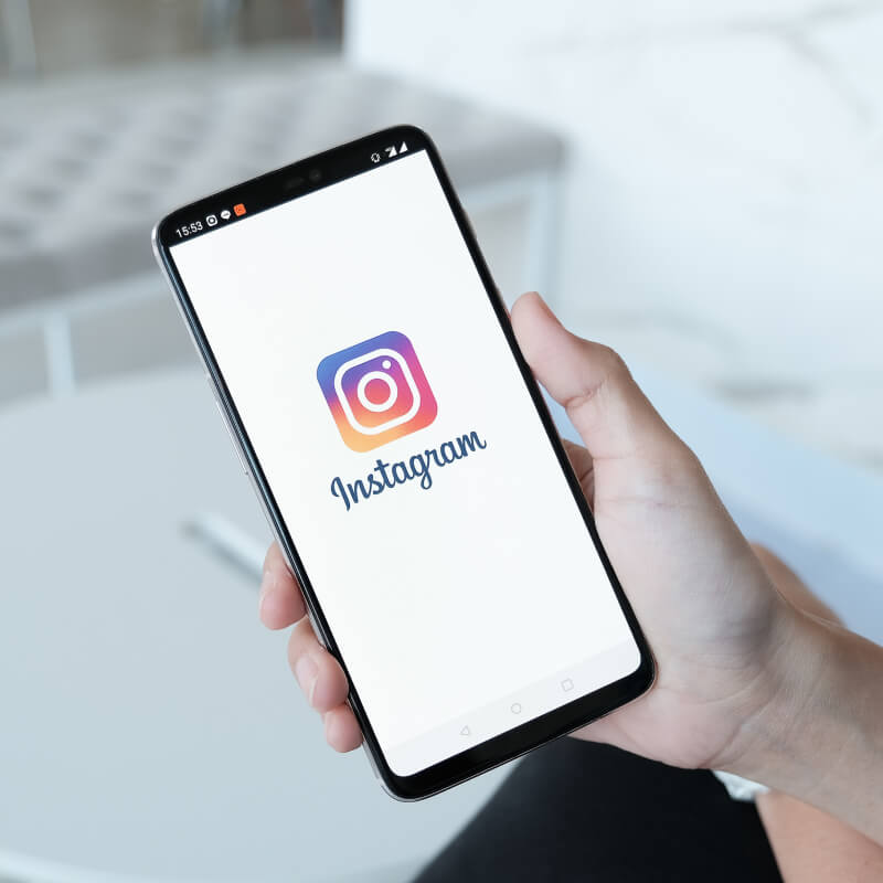 Telefon z logo Instagrama, trzymany w ręce, na białym tle