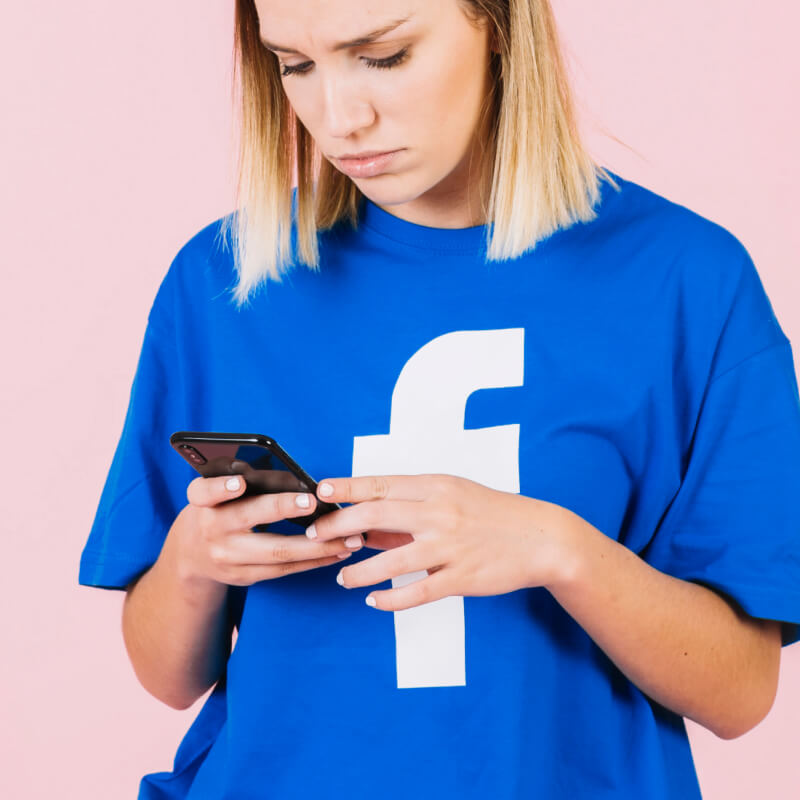 Osoba w koszulce z logo Facebooka, trzymająca telefon