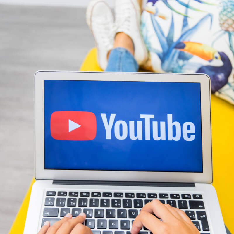 Osoba, trzymająca na kolanach laptop z logo YouTube.