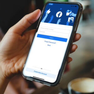 Telefon z ekranem logowania do Facebooka, trzymany w ręce.