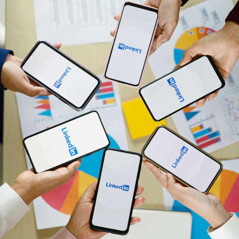 Grupa osób trzymająca nad stołem telefony logo LinkedIn