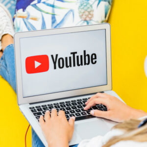 Laptop z logo YouTube na tle żółtej kanapy