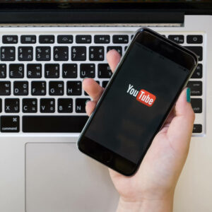 Osoba trzymająca telefon z logo YouTube na tle komputera