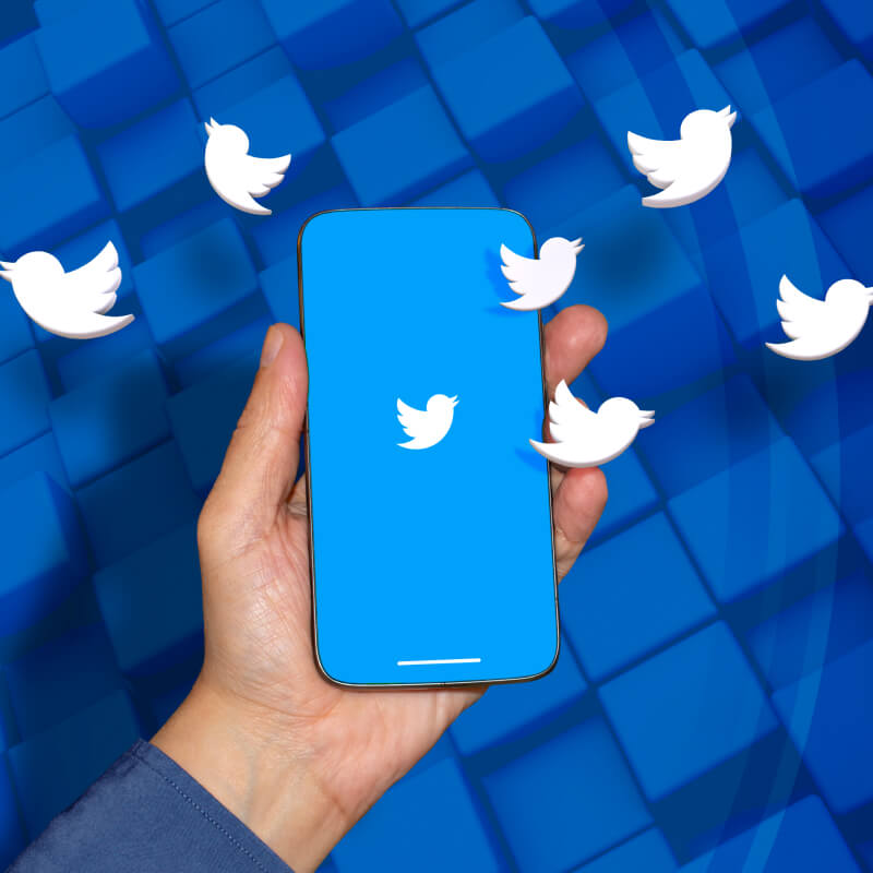 Osoba trzymająca telefon z logo Twittera, na niebieskim tle