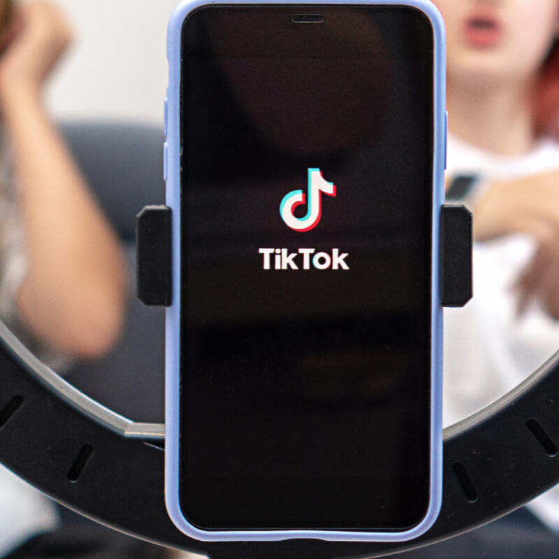 Telefon z logo aplikacji TikTok na tle dwóch osób
