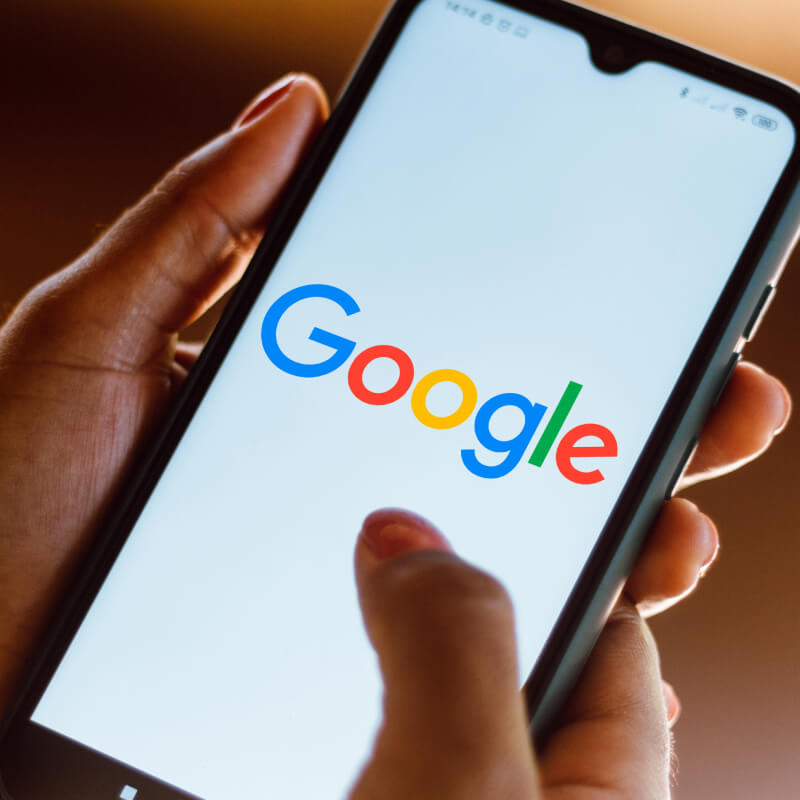 Osoba trzymająca w dłoniach telefon z logo Google