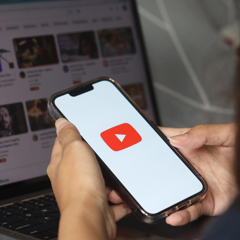 Osoba trzymająca telefon z logo YouTube na tle laptopa