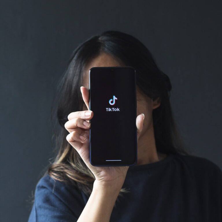 Osoba, zasłaniająca twarz telefonem z logo TikToka