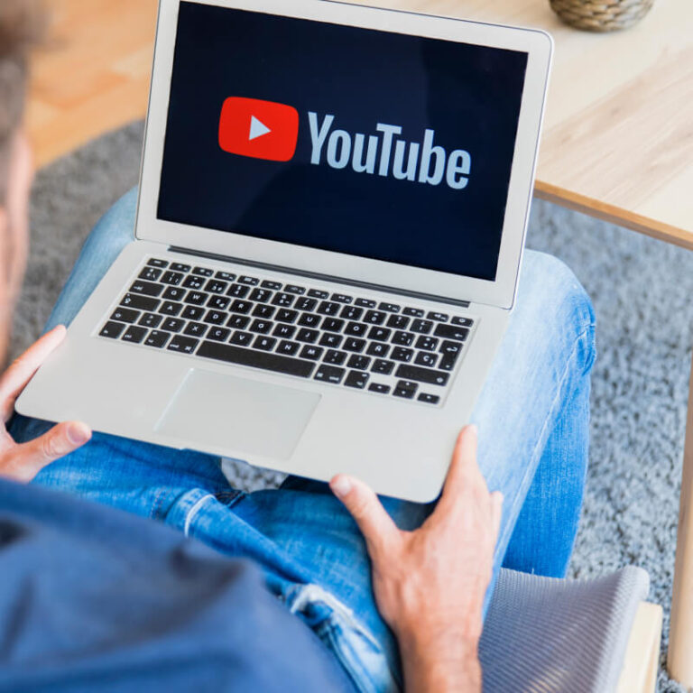 Osoba trzymająca na kolanach laptop z logo YouTube
