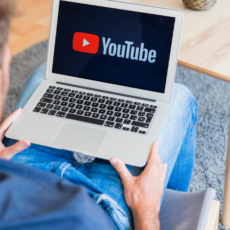 Osoba trzymająca na kolanach laptop z logo YouTube