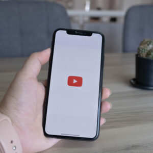 Osoba trzymająca w dłoni telefon z logo YouTube na tle biurka