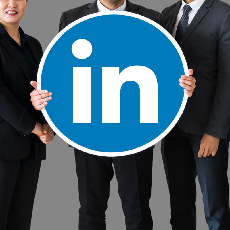 Osoby w garniturach trzymające w dłoniach okrągłe logo LinkedIn