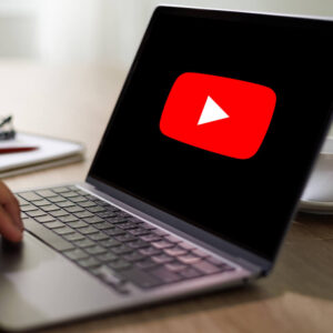 Laptop z logo YouTube na ekranie stojący na drewnianym biurku