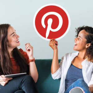 Dwie osoby siedzące na kanapie, jedna trzyma w dłoni logo platformy Pinterest