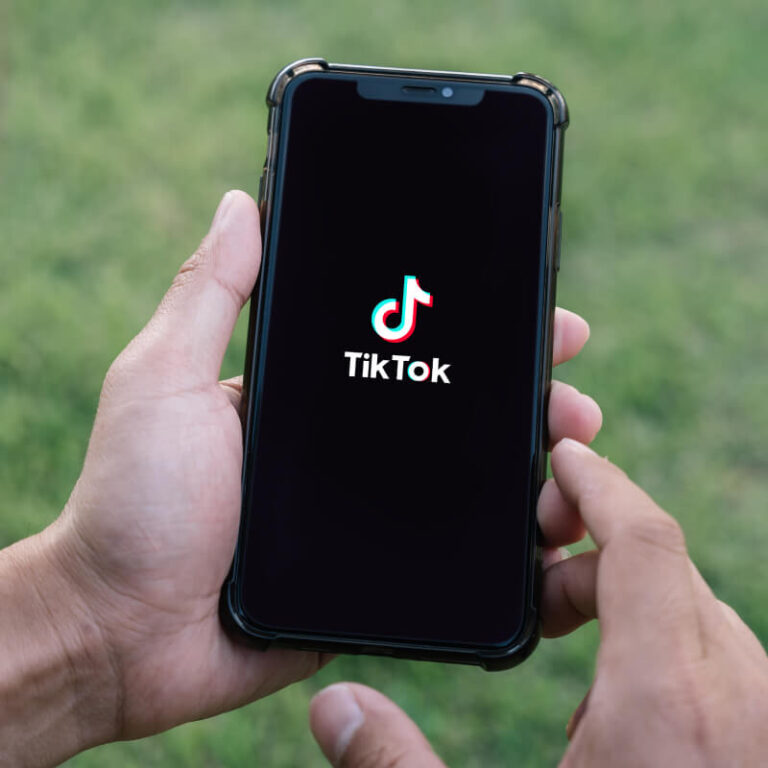 Osoba trzymająca telefon z logo TikToka na ekranie, na tle zielonej trawy