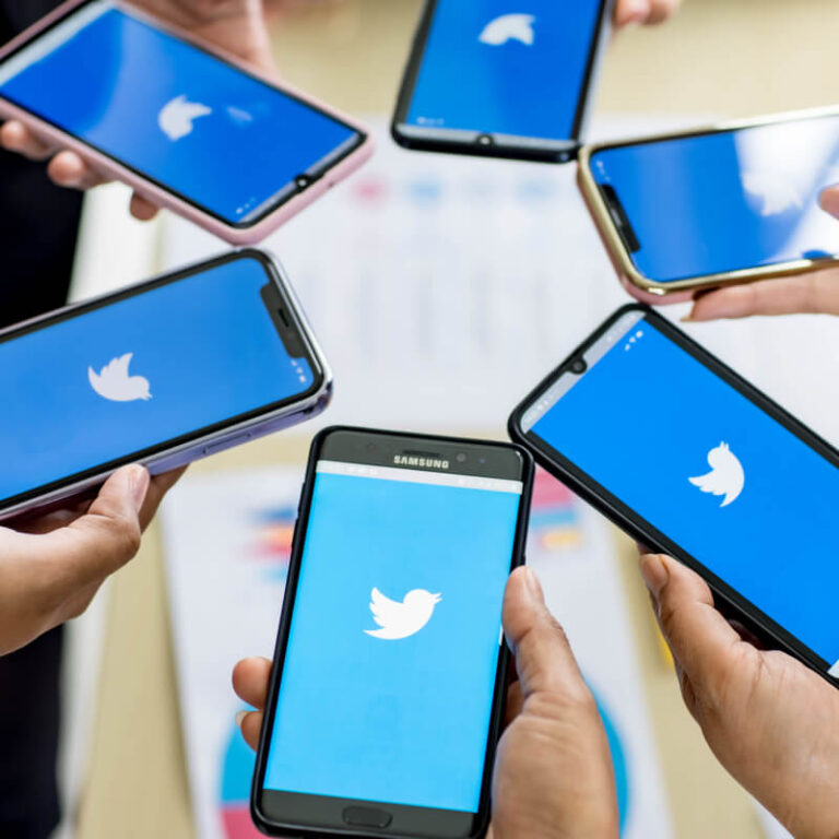 Grupa osób stojąca w kole z telefonami z logo Twittera w dłoniach
