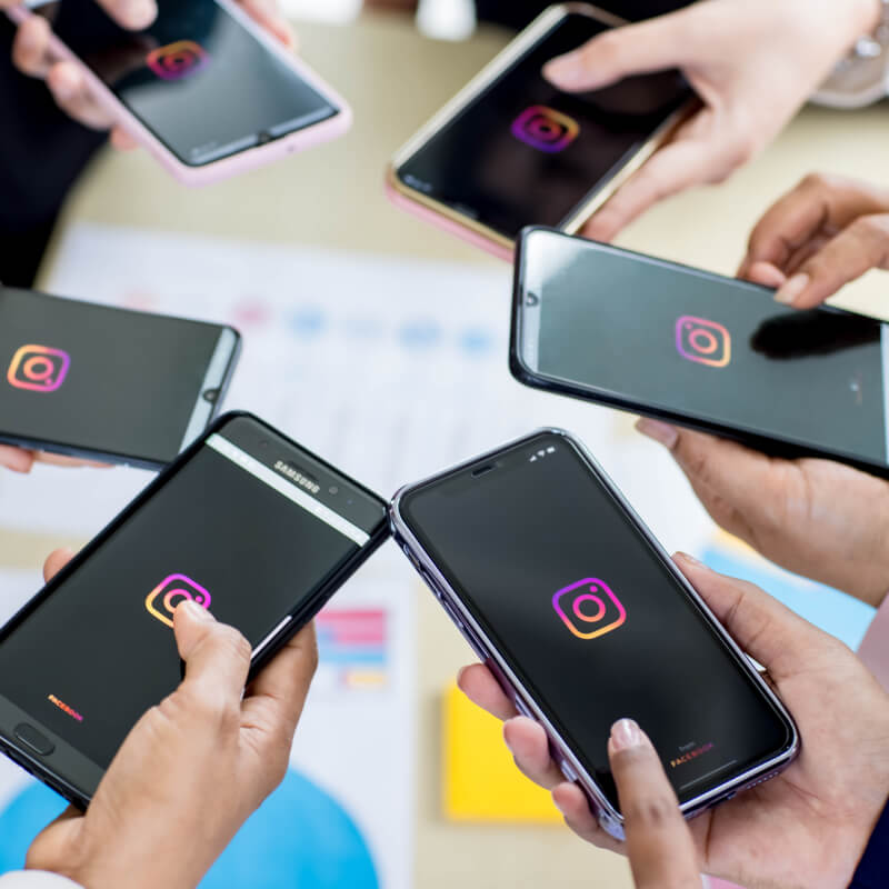 Zdjęcie grupy osób, stojącej w kole, z telefonami z logo aplikacji Instagram na ekranie.