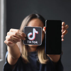Osoba trzymająca przed twarzą telefon i logo aplikacji TikTok