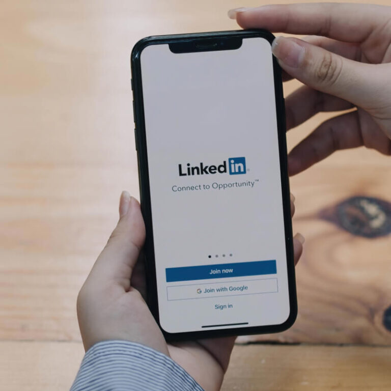 Telefon z logo LinkedIn trzymany w dłoniach na tle biurka