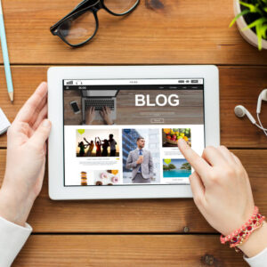 Tablet wyświetlający blog, trzymany w dłoniach, na tle biurka