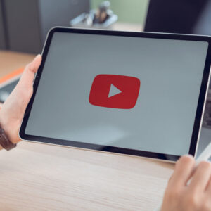 Tablet z logo YouTube trzymany w dłoniach na tle biurka