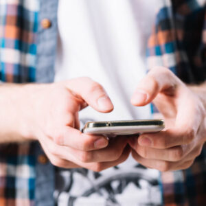 Osoba ubrana w koszulę, trzymająca w dłoniach telefon,