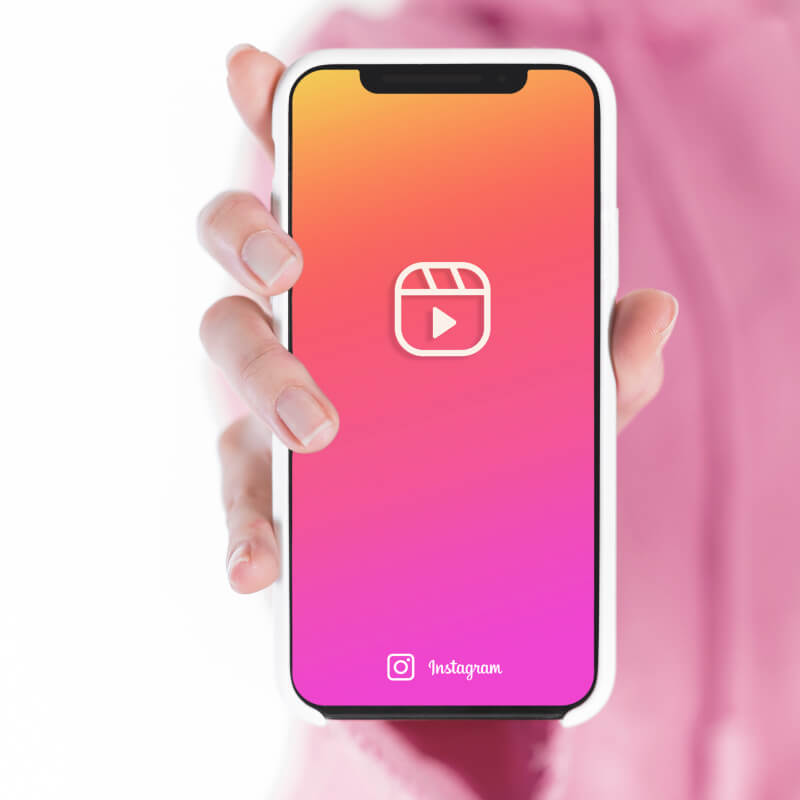 Osoba w różowej koszuli trzymająca w dłoni telefon z logo Instagram Reels