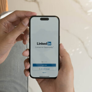 Telefon z ekranem logowanie do LinkedIn trzymany w dłoni, na tle marmuru