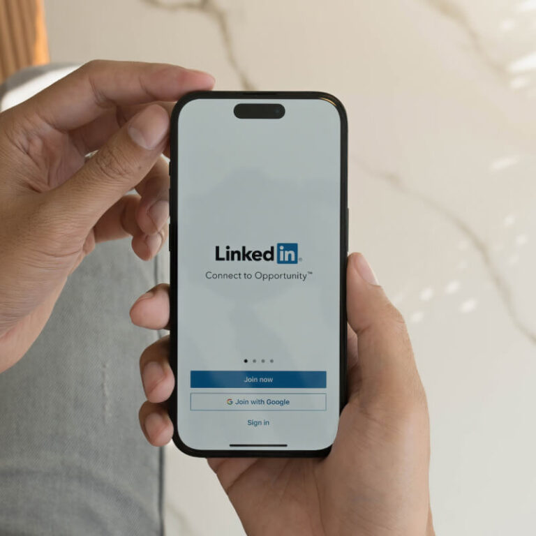 Telefon z ekranem logowanie do LinkedIn trzymany w dłoni, na tle marmuru
