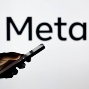 Osoba trzymająca w dłoni telefon na tle logo Meta