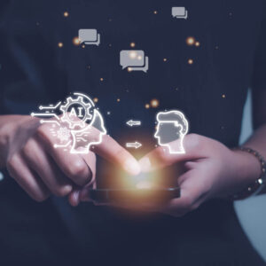 Osoba trzymająca w dłoniach telefon, z grafikami przedstawiającymi człowieka, sztuczną inteligencję i dymki czatu nad ekranem