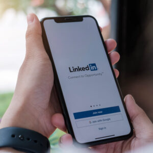 Osoba trzymająca w dłoniach telefon z ekranem logowania do LinkedIn na wyświetlaczu