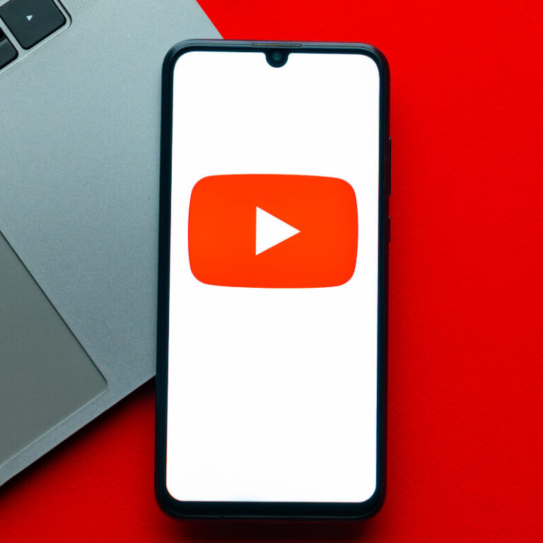 Telefon z logo YouTube leżący na laptopie, na czerwonym tle