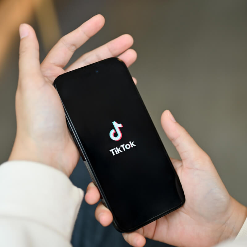 osoba trzymająca w dłoni telefon logo aplikacji TikTok