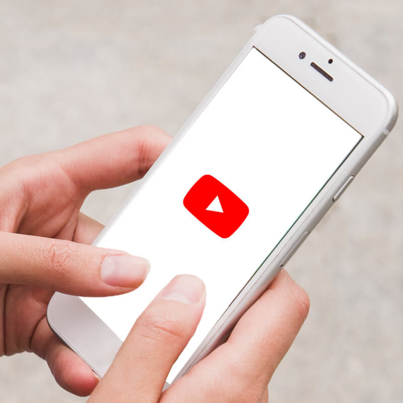 Osoba trzymająca w dłoniach telefon z logo aplikacji YouTube na ekranie