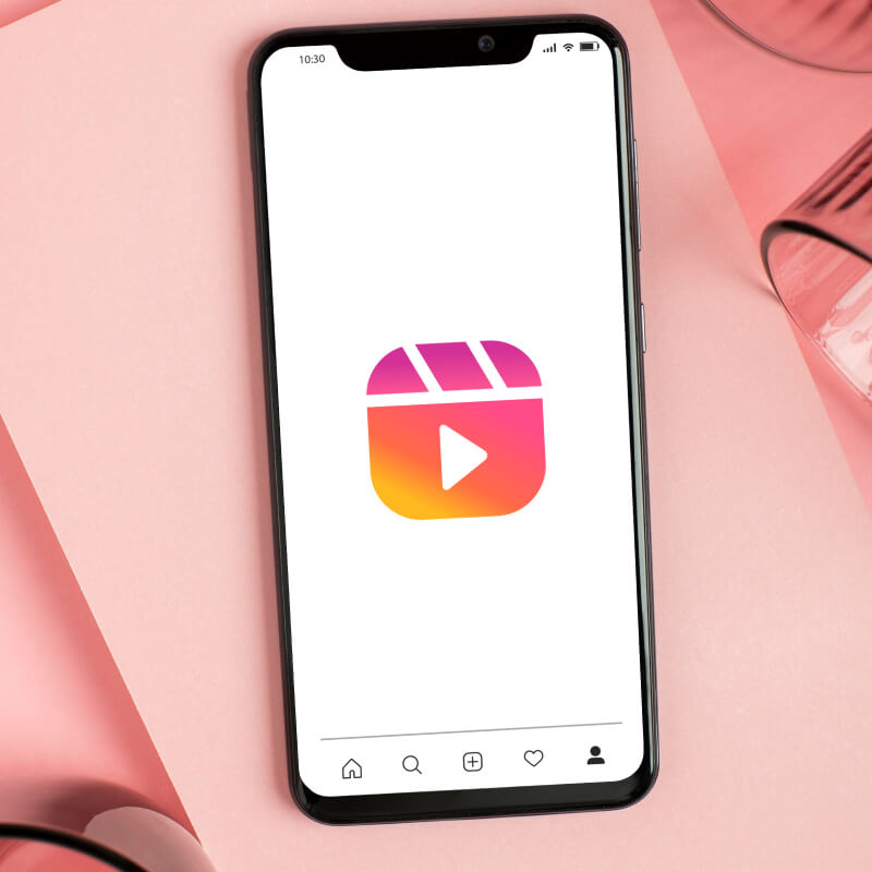 Telefon z logo Instagram Reels na ekranie na różowym tle