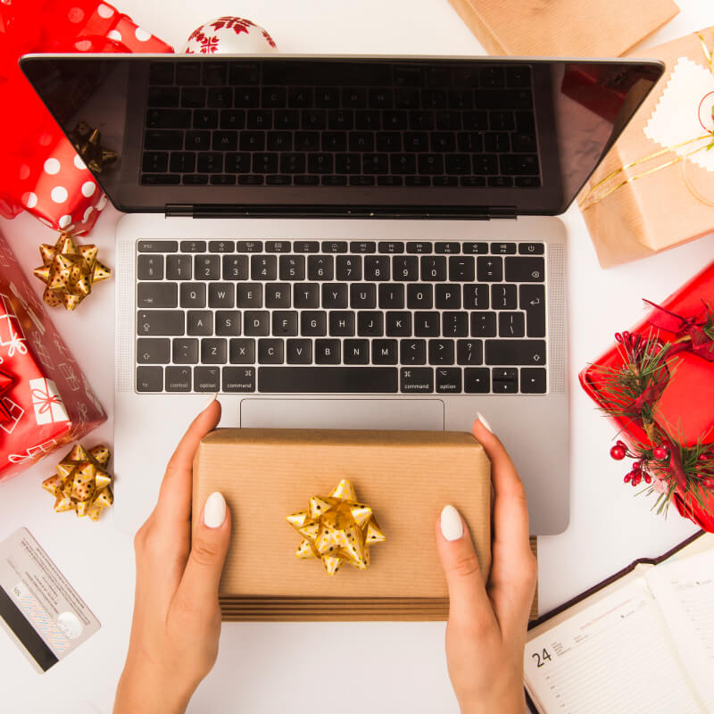 Osoba trzymająca w dłoniach prezent świąteczny na laptopie