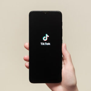 Osoba trzymająca w dłoni telefon z logo TikToka na beżowym tle
