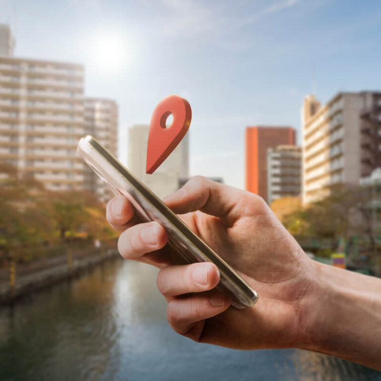 Osoba trzymająca w dłoni telefon z ikoną lokalizacji nad nim, na tle miasta