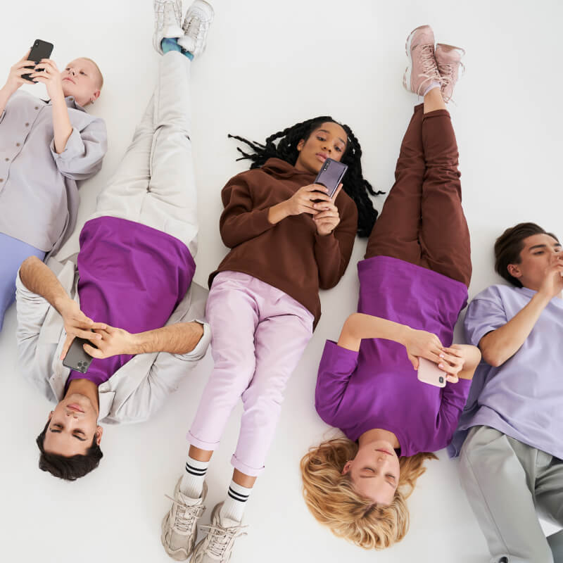 Grupa nastolatków leżąca na podłodze z telefonami w dłoniach