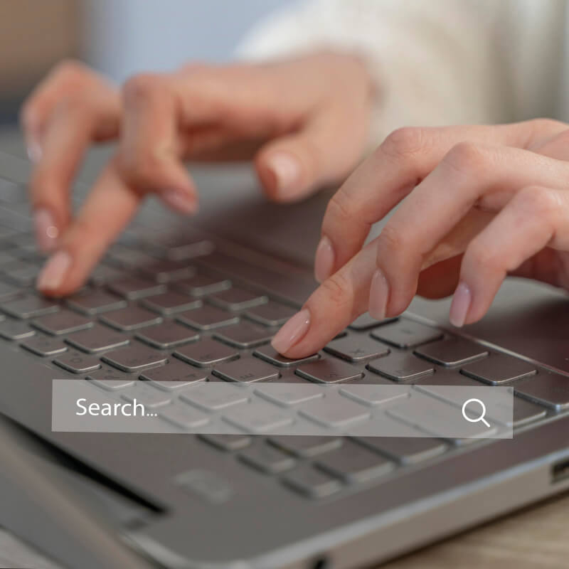 Pasek wyszukiwarki Google na tle osoby piszącej coś na klawiaturze laptopa