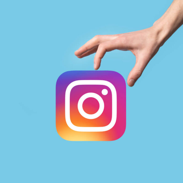 Logo aplikacji Instagram trzymane w dłoni, na niebieskim tle