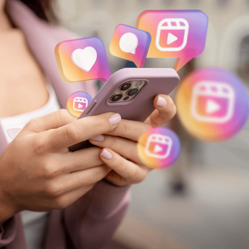 Ikony z aplikacji Instagram otaczające telefon trzymany w dłoniach