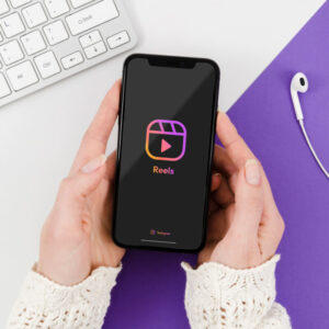 Osoba trzymająca nad biurkiem telefon z logo Rolek aplikacji Instagram