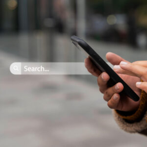 Osoba trzymająca telefon na tle paska wyszukiwarki Google